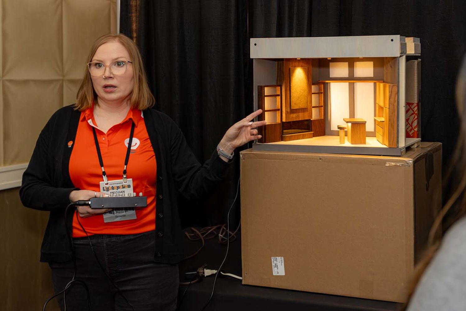 woman from Light Can Help You in orange shirt explaining light diorama